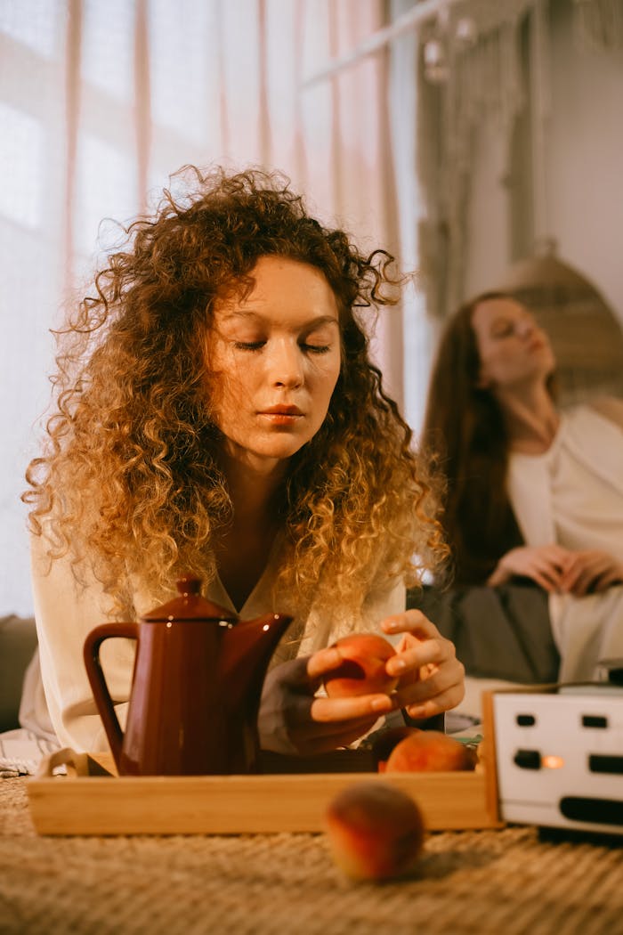 Two women enjoying a cozy indoor setting with peaches and tea in soft morning light.