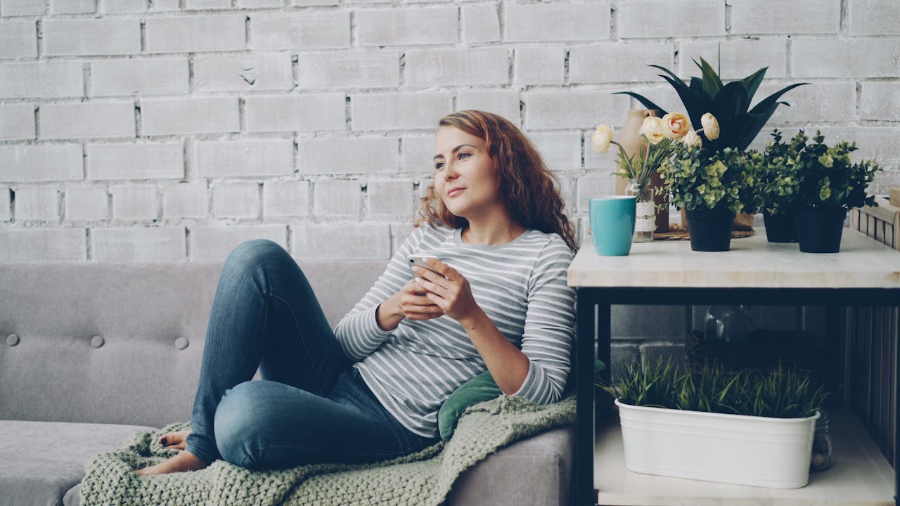 services-01 A woman enjoys a relaxing moment on a couch with plants nearby, exuding calm.